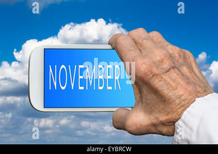 Smart phone in old hand with month of the year - November on screen. Selective focus. Stock Photo