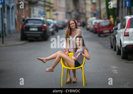 Two young girls girlfriend. Conceptual photo, a teen girl sits on a chair in the middle of the street, her friend stands behind Stock Photo