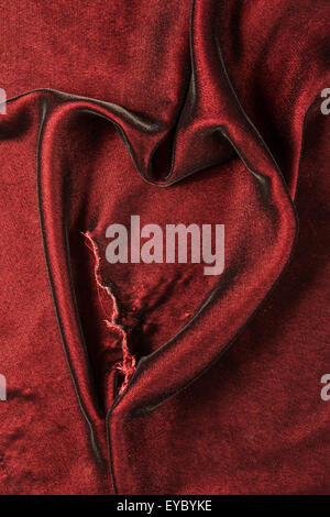 Burgundy velvet fabric with a tear in it, pulled into a heart shape Stock Photo