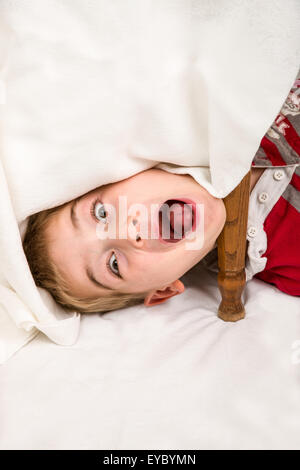 Six year old boy having fun making faces under a covered table Stock Photo
