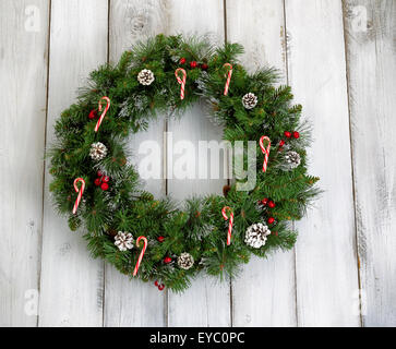 Christmas wreath decorated with pine cones, candy canes, and red berries on rustic white wooden boards. Stock Photo