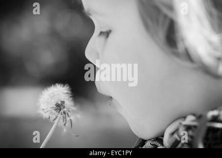 Caucasian blond baby girl and dandelion flower in a park, monochrome photo with selective focus Stock Photo