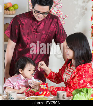 Chinese New Year, reunion dinner. Happy Asian Chinese family with red cheongsam dining at home. Stock Photo