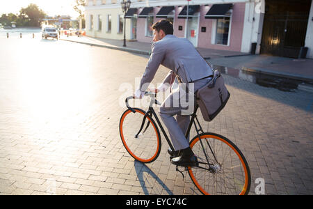 Businessman riding bicycle to work on urban street in morning Stock Photo