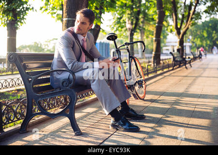 Young businessman sitting on the bench in city park and looking away Stock Photo