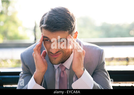 Portrait of a businessman sitting on the bench outdoors and having headache Stock Photo