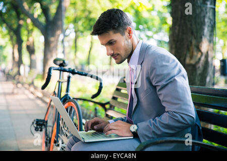 Handsome businessman sitting on the bench outdoors and using laptop Stock Photo