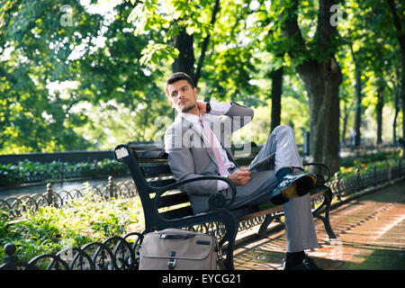 Thoughtful businessman sitting on the bench with tablet computer and looking away Stock Photo