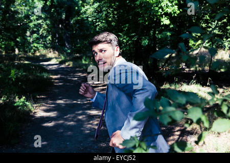 Frightened businessman running away from something outdoors in park Stock Photo