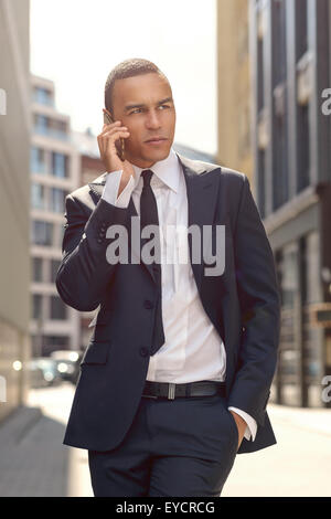 Three Quarter Shot of a Gorgeous Young Businessman Talking to Someone on his Mobile Phone While Walking In the Street and Lookin Stock Photo