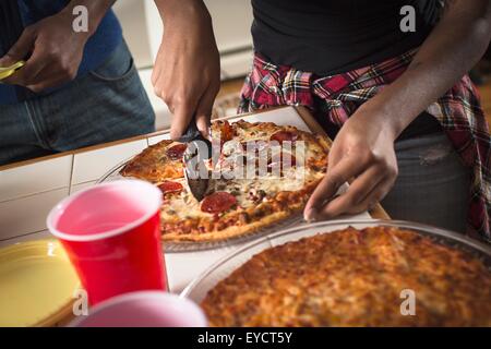 Cropped close up of womans hands cutting pizza in kitchen Stock Photo