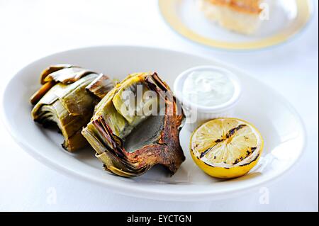 Grilled artichokes with lemon on restaurant table Stock Photo