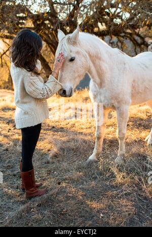 Young woman petting white horse in field Stock Photo