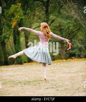Rear view of young female dancer poised holding red high heels in park Stock Photo