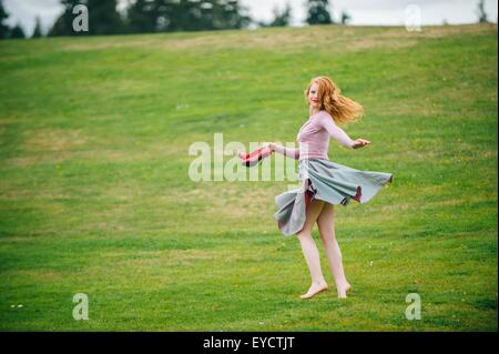 Portrait of young woman dancing in park holding red high heels Stock Photo