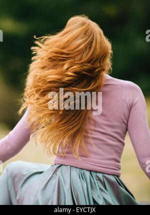 Rear view of young woman with long red hair twirling in park Stock Photo