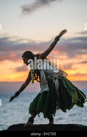 Woman hula dancing on coastal rocks wearing traditional costume at sunset, Maui, Hawaii, USA Stock Photo