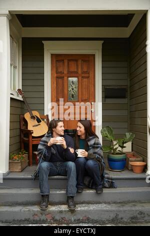 Young couple sitting on porch step chatting Stock Photo