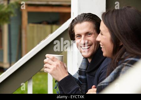 Young couple sitting on porch step drinking coffee Stock Photo