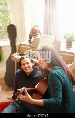 Young couple playing acoustic guitar in living room Stock Photo
