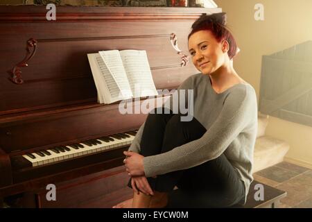 Portrait of young woman sitting on piano stool hugging knees