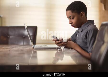 Teenage boy at dining table reading smartphone texts Stock Photo