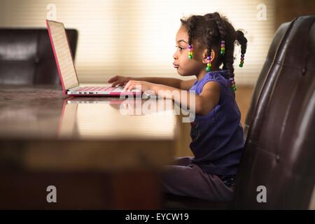 Cute girl at dining table using laptop Stock Photo