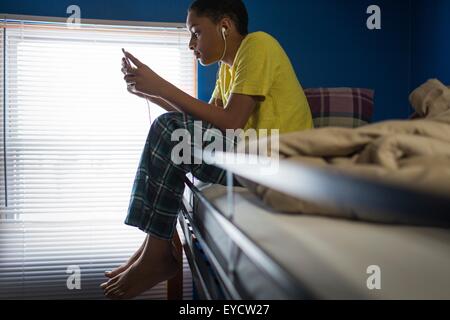 Teenage boy sitting on bunkbed reading smartphone texts Stock Photo