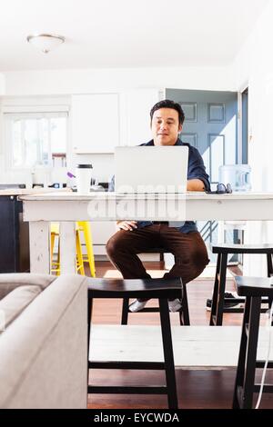 Mature businessman typing on laptop at kitchen table Stock Photo