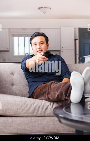 Mature man on sofa switching on remote control Stock Photo