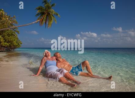 Senior couple relaxing on beach, Maldives Stock Photo