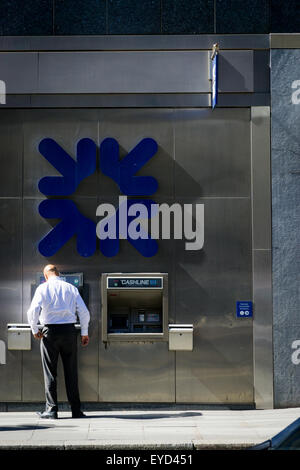 A shirt sleeved man using a Royal Bank of Scotland (RBS) cash machine in the City of London UK. Late afternoon summer sun. Stock Photo