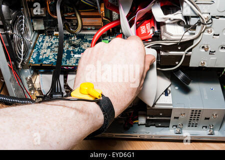 Hand with yellow static strap connected, reaching into the inside of a desktop computer and connecting ribbon cable to hard drive. Stock Photo