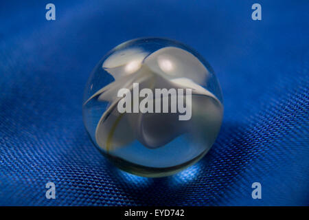 Clear glass globe with abstract white pattern resting on blue fabric. Stock Photo