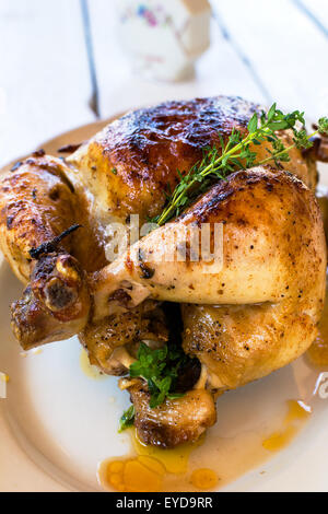 Whole roast chicken in a white plate on a white wooden table Stock Photo