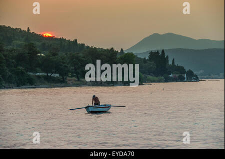 A fisherman tends to his nets in a little fishing boat as the sun goes down Stock Photo