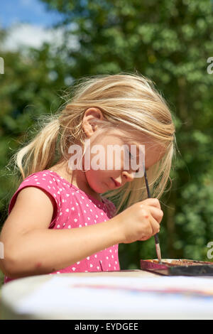A girl painting with water colours (watercolors), painting a paper plate with watercolour paints outside in garden Stock Photo