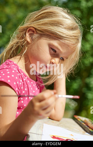 A girl painting with water colours (watercolors), painting a paper plate with watercolour paints outside in garden Stock Photo