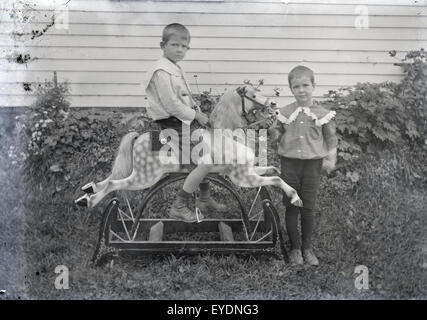 Antique c1900 photograph of two boys, probably brothers or twins, showing off their new Victorian rocking horse. Location is USA. Stock Photo