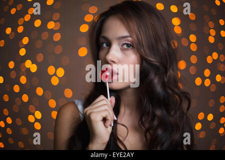Pretty brunette with curly hair eating lollipop on sparkling background Stock Photo