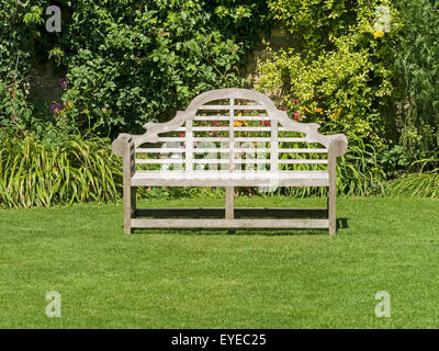 Ornate wooden garden bench seat on green lawn, Barnsdale Gardens, Rutland, England, UK Stock Photo