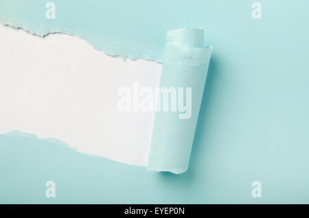 Tear in a piece of blue paper revealing white background underneath Stock Photo