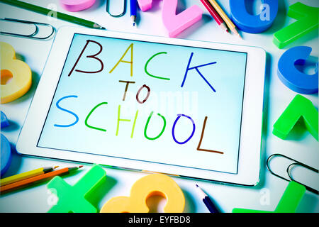 the sentence back to school handwritten in a tablet computer, placed on a table full of pencils and numbers of different colors, Stock Photo