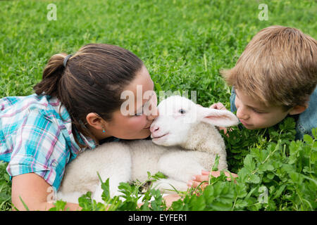 Boy (10-11) with girl (12-13) kissing lamb Stock Photo