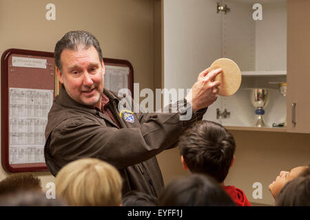 In the sacristy of a Laguna Niguel, CA, Catholic church, an Extraordinary Minister of the Holy Eucharist shows communion wafer to multiracial child parishioners in preparation for their First Communion, also known as Holy Eucharist. Note Knights of Columbus logo on jacket. Stock Photo