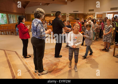 At a Laguna Niguel, CA, Catholic church, a Vietnamese American priest demonstrates marching in procession to receive communion child parishioners in preparation for their First Communion, also known as Holy Eucharist. Note woman volunteer. Stock Photo