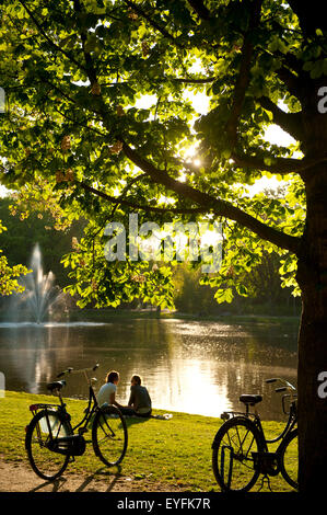 Couple relaxing beside lake in the Vondelpark in the evening; Amsterdam, Holland Stock Photo