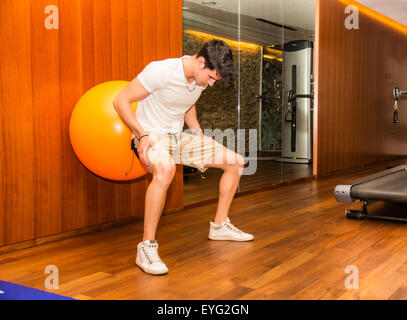 Attractive young man working out with exercize ball against wall to train abs Stock Photo