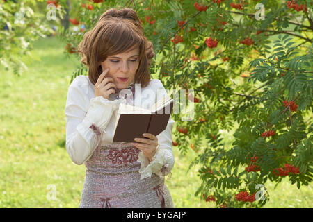 Smiling girl reads interesting book near rowan tree in summer Stock Photo