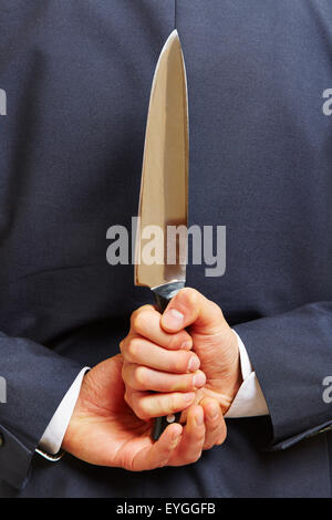 Hand of a business man holding a big knife behind his back Stock Photo